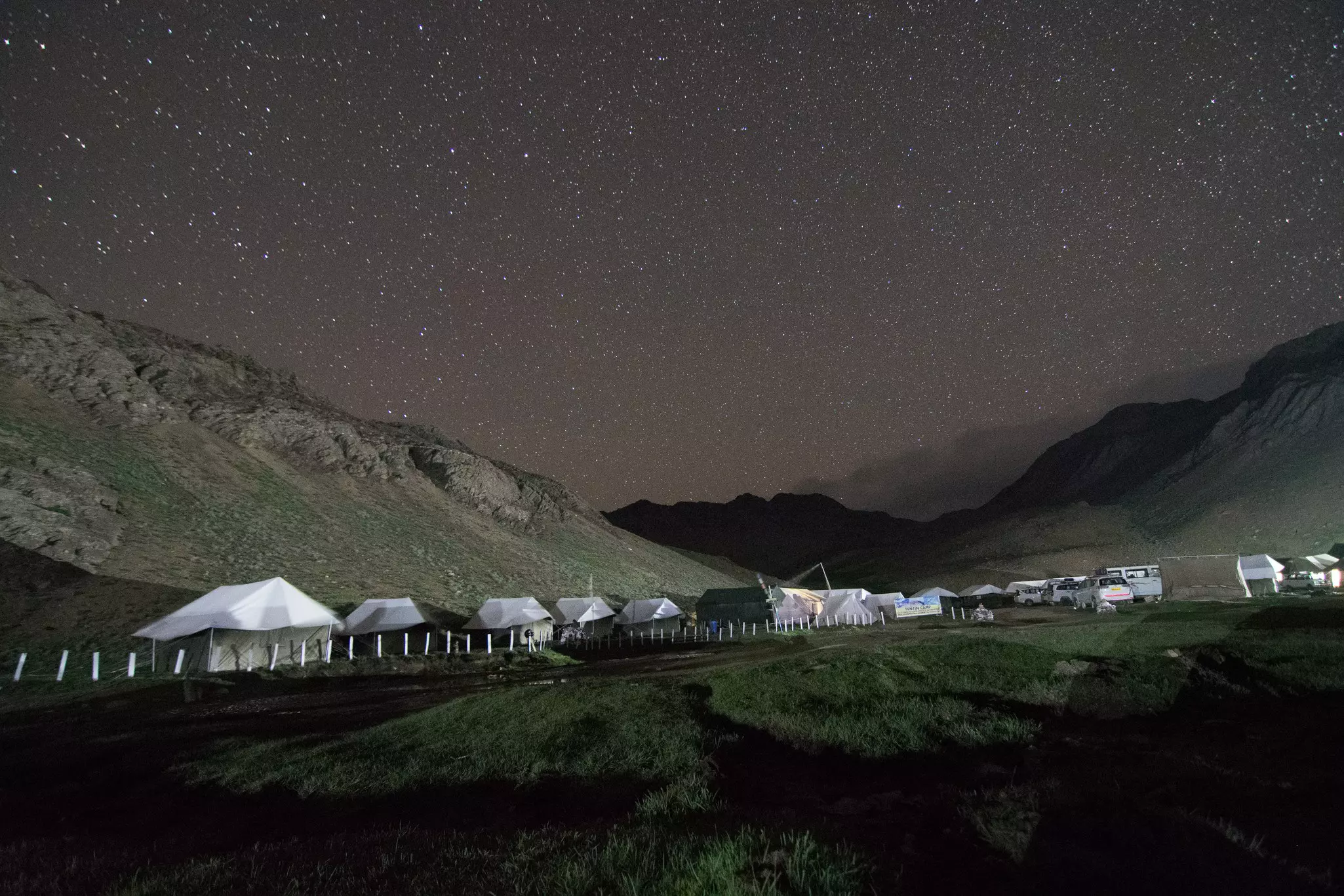 A starry sky is seen above a campsite with large tents in the mountains.
