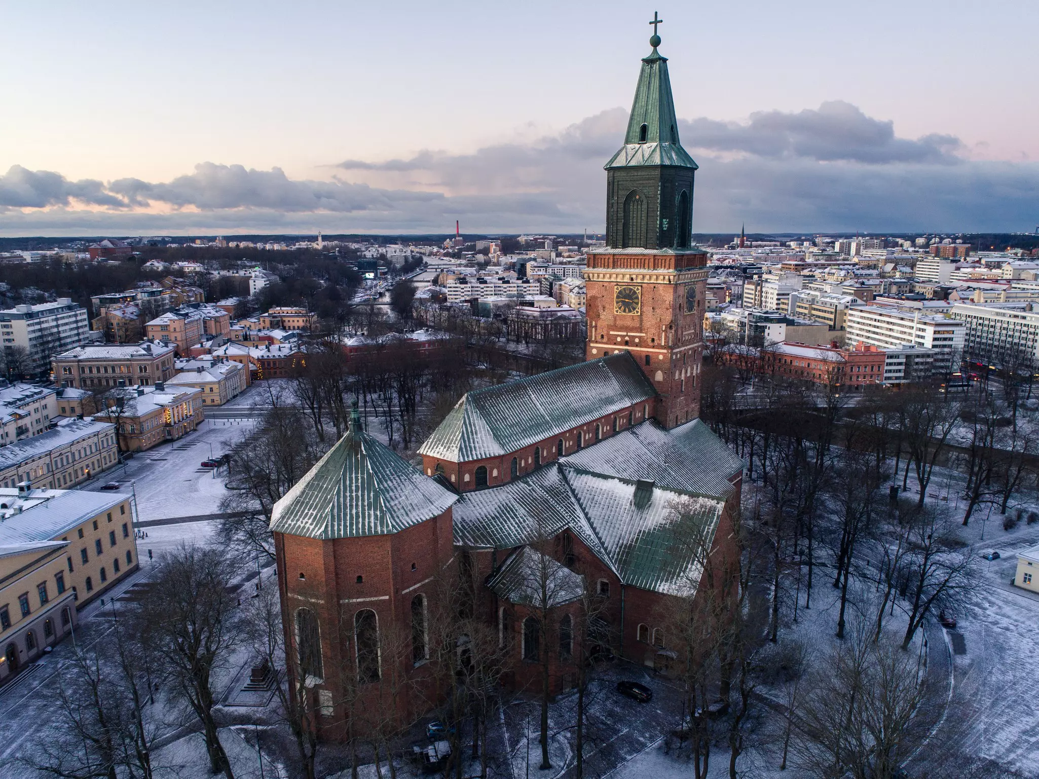 A high-angle aerial view of a cathedral in a city, with a dusting of snow visible on the ground.
