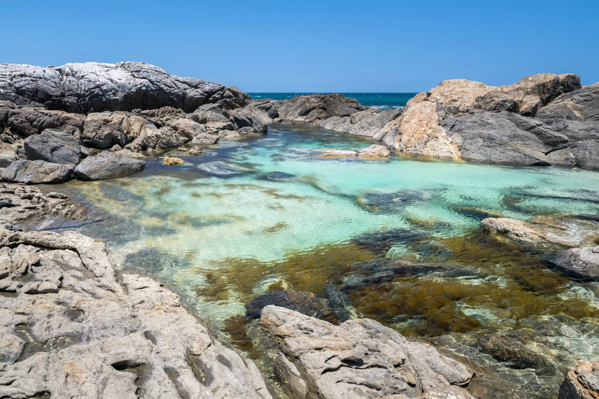 A turquoise pool of water surrounded by rocks keeping it separate from the nearby ocean.