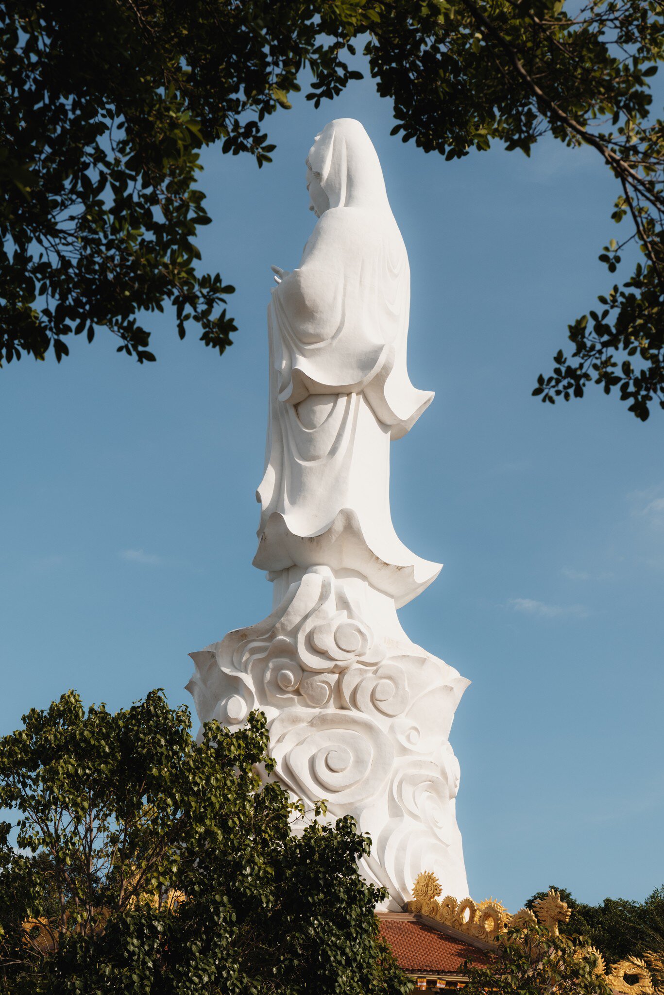View of the statue atop the Ho Quoc Pagoda framed by branches on Phu Quoc Island, Vietnam.