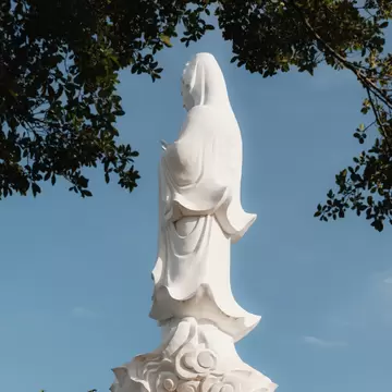 View of the statue atop the Ho Quoc Pagoda framed by branches on Phu Quoc Island, Vietnam.