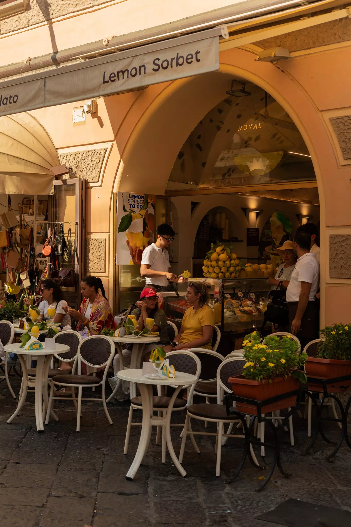 Women eating lemon sorbets at a gelato shop with small tables clustered closely under an awning