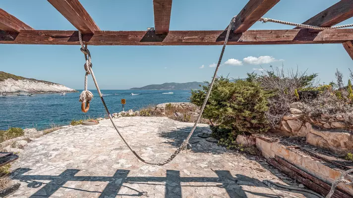 A rope swing on a stone patio overlooking a blue sea