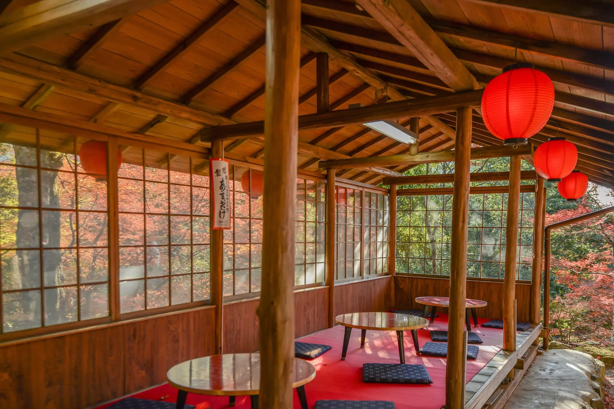 An open-sided structure with three low wooden tables and several cushions on the floor for kneeling on