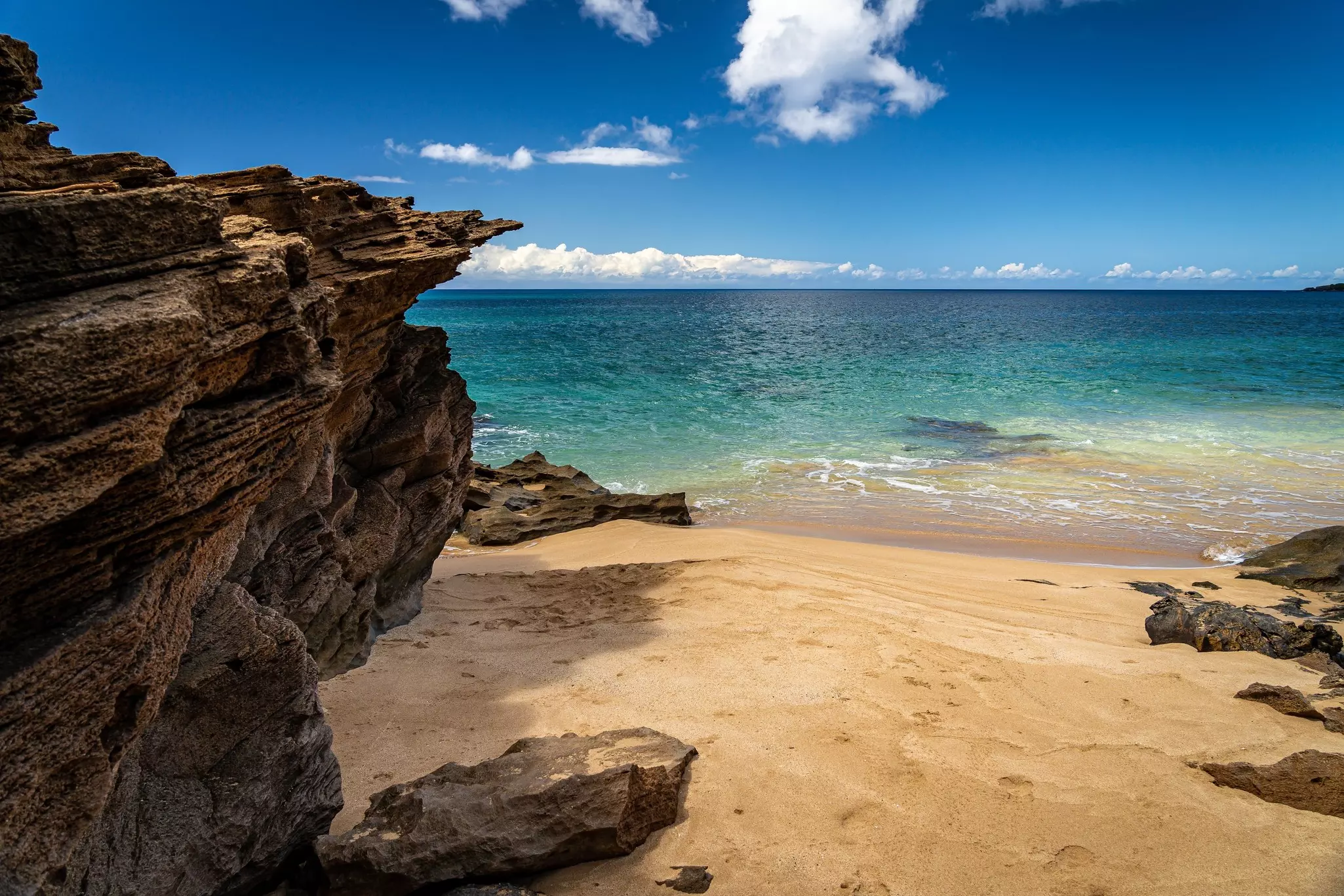 Jagged rocks with a small sandy beach and the ocean in the distance on a sunny day.