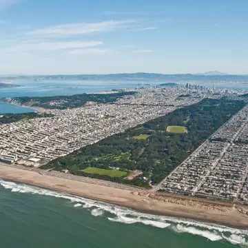 An aerial view of Golden Gate Park from the Pacific Ocean with the Golden Gate Bridge in the background.