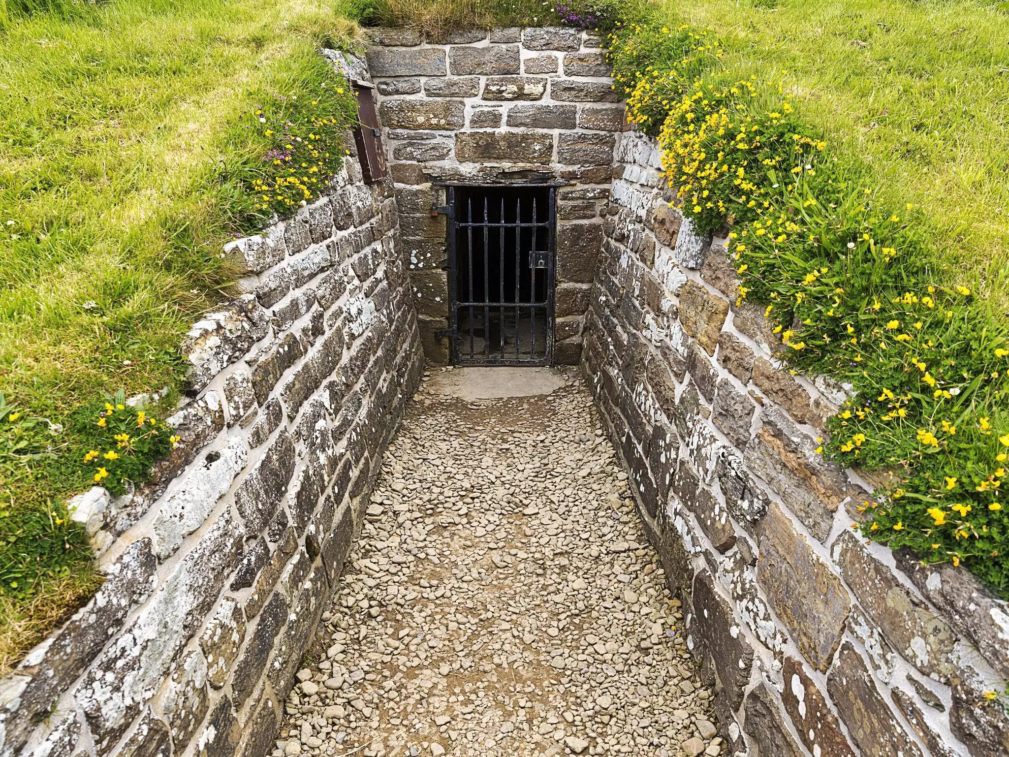 A small outdoor passageway between stone walls leading to the door to a tomb