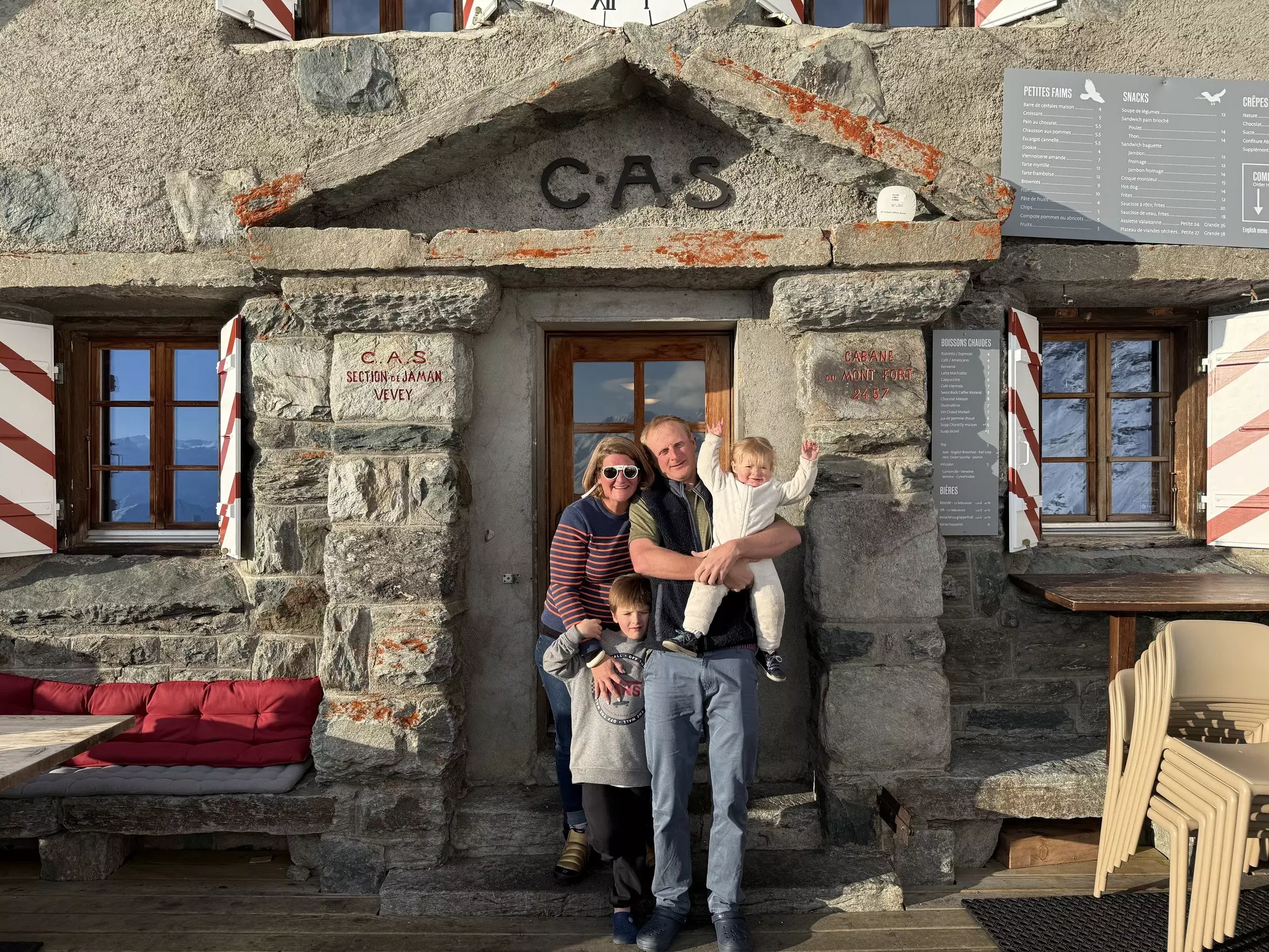 A man and woman holding their young children in front of a stone building