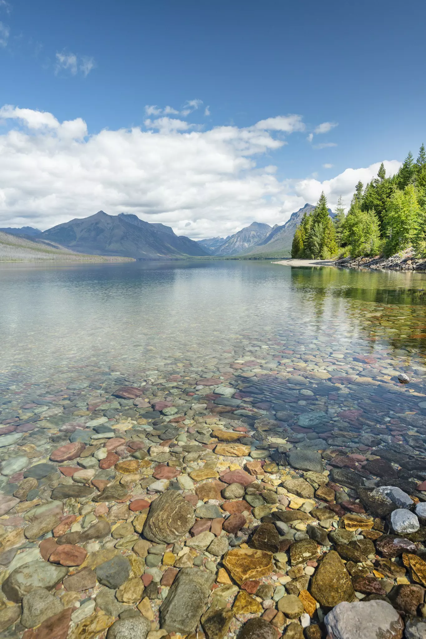 A lake, with shallow water so clear that colorful pebbles at the bottom of the lake are evident.