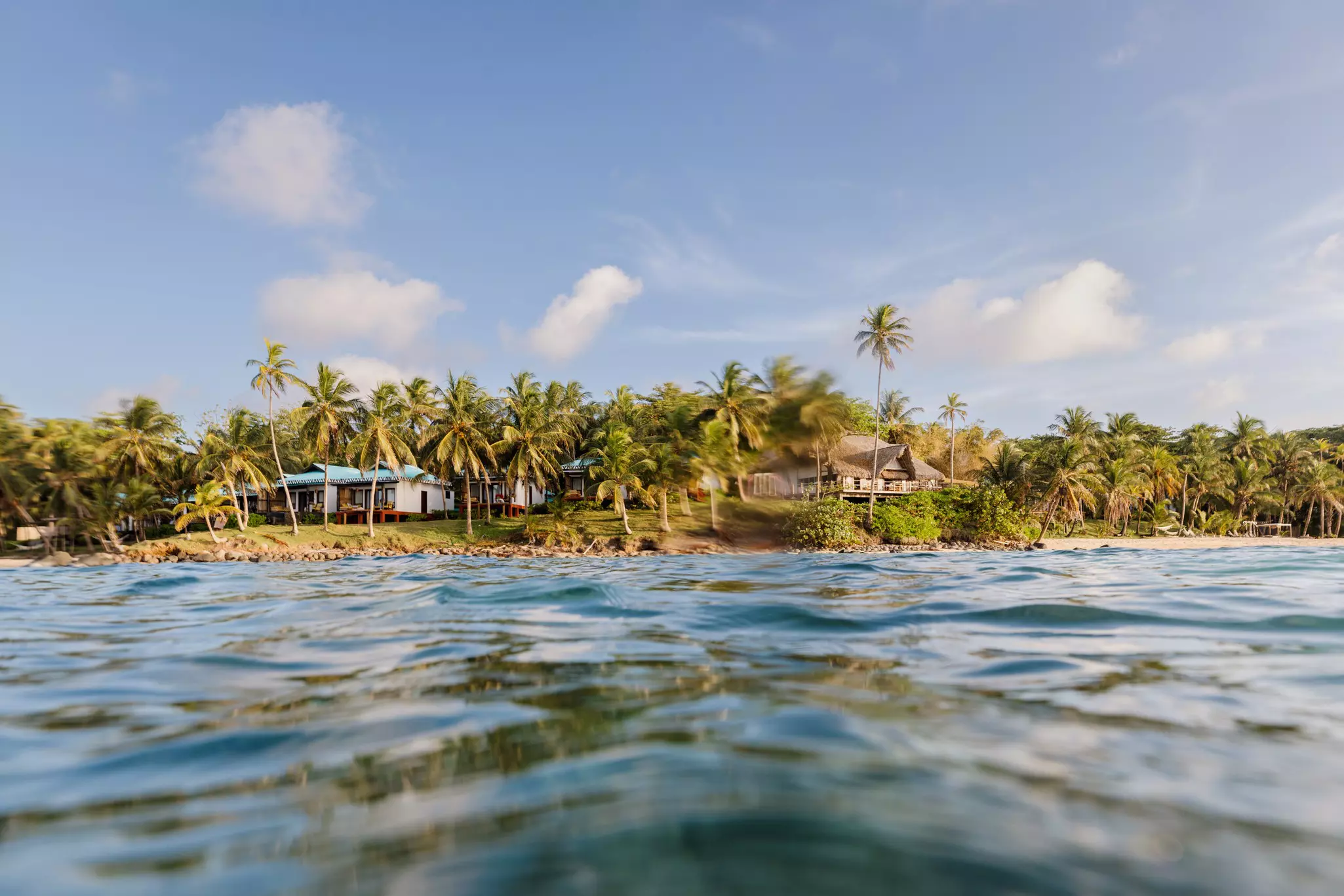 A palm-fringed island with small bungalows viewed from the ocean.