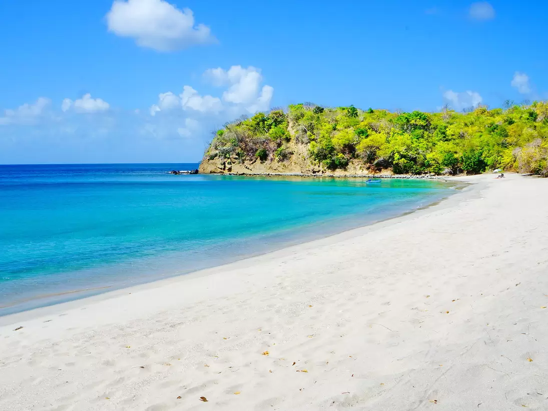 An empty white-sand cove curving to a wooded headland, with clear blue water shading to turquoise in the shallows.