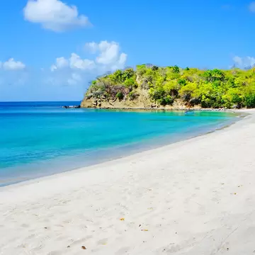 An empty white-sand cove curving to a wooded headland, with clear blue water shading to turquoise in the shallows.