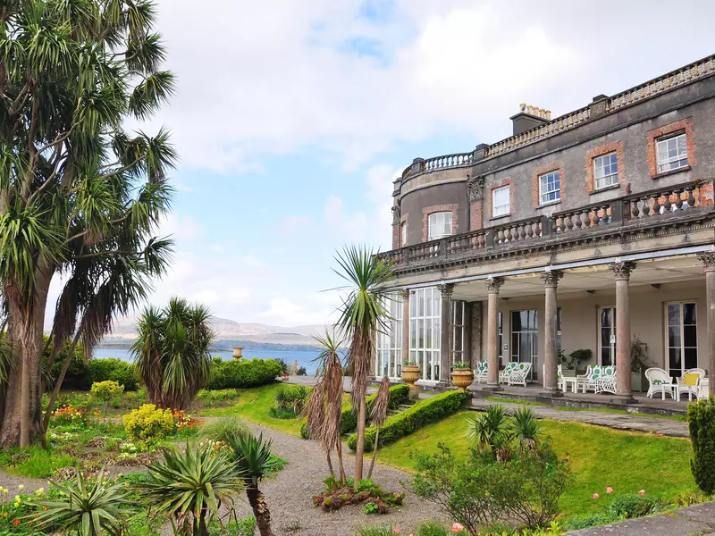 A large estate home with a terrace with the sea in the background. 