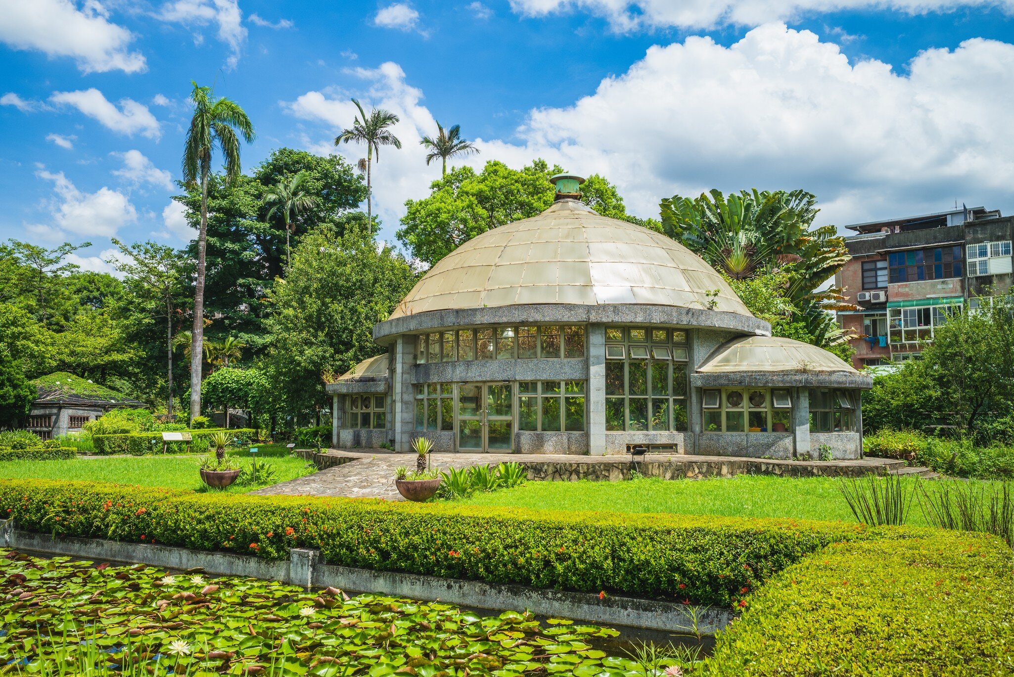 The greenhouse in Taipei's Botanical Garden surrounded by bright green trees and a lily pond in front.