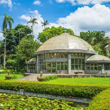 The greenhouse in Taipei's Botanical Garden surrounded by bright green trees and a lily pond in front.