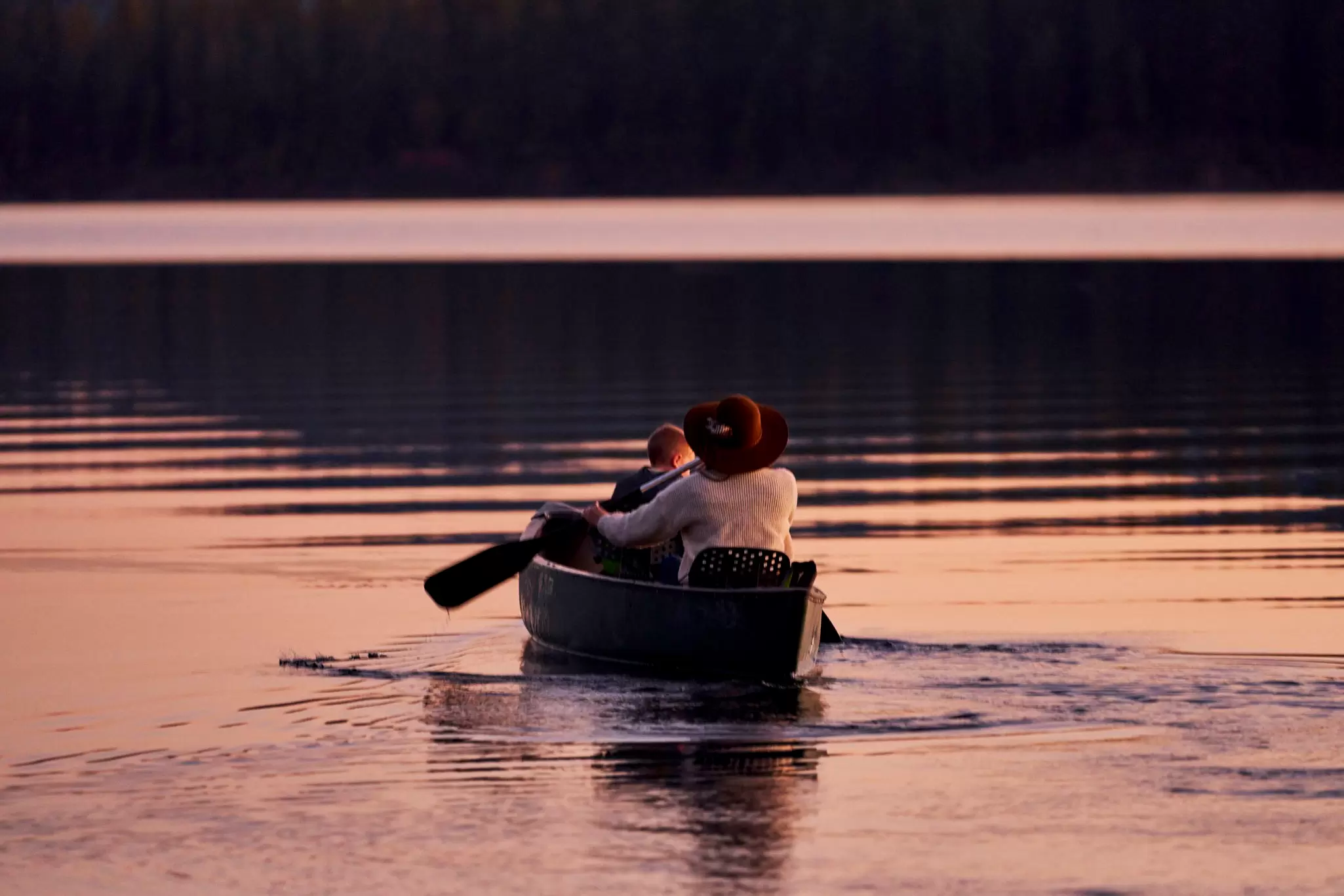 An adult and child in a canoe on a calm lake at sunset.