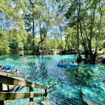 Tubers and swimmers float in shallow clear aqua spring waters on a hot sunny summer's day.