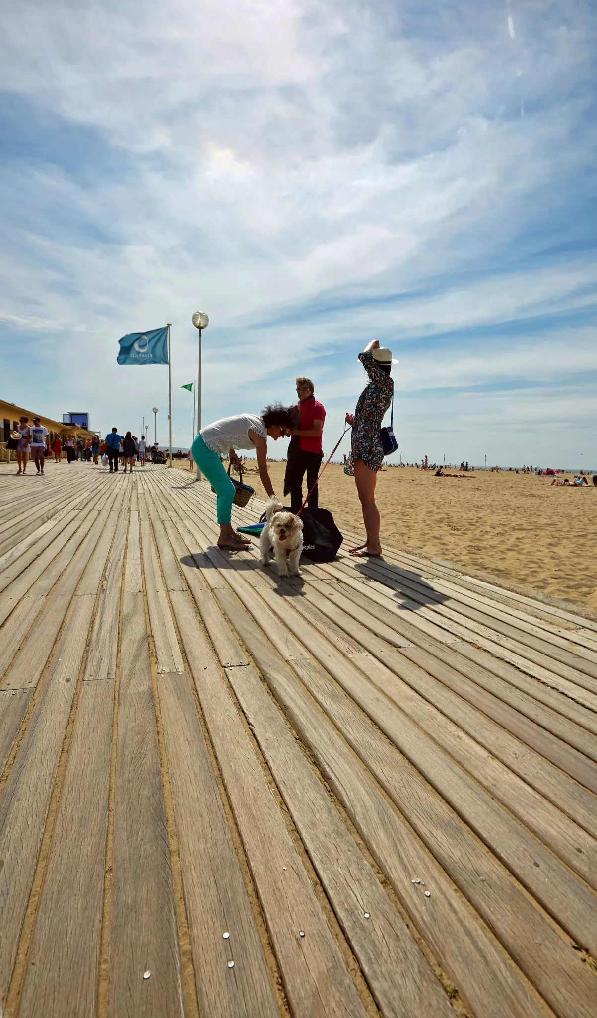 Three people and dog standing on beach promenade at Deauville on the wooden promenade alongside the beach.