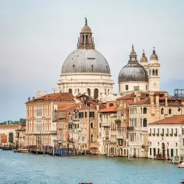 Pastel-colored buildings line a canal; an imposing church rises above the skyline.