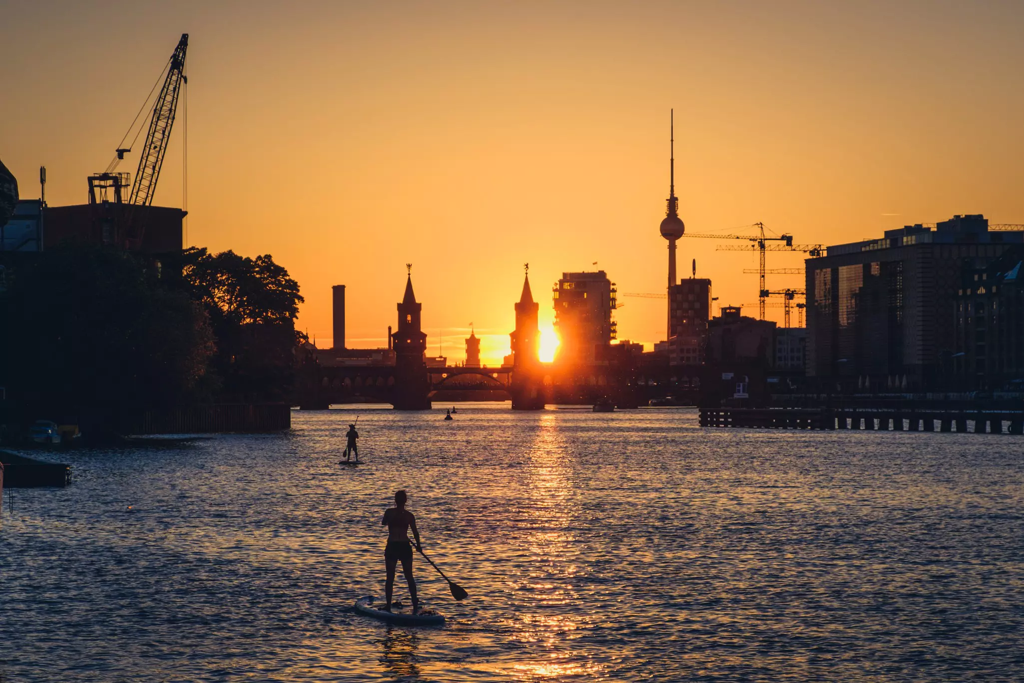 Paddleboarders on a river as the the sunset throws all the surrounding buildings and the bridge into silhouette