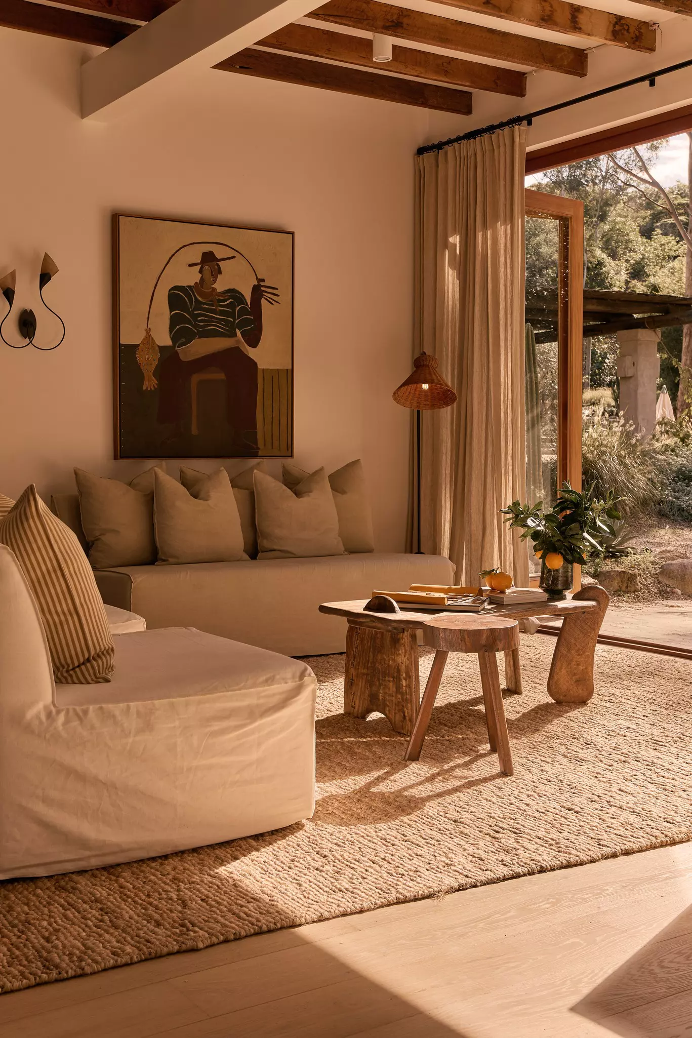 An earth-toned room with a wood table and cushiony couches bathed in sunlight