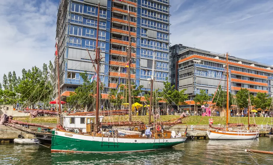 Traditional wooden sailing ships moored in Kiel harbour, Germany, before modern blue and orange glass office blocks
