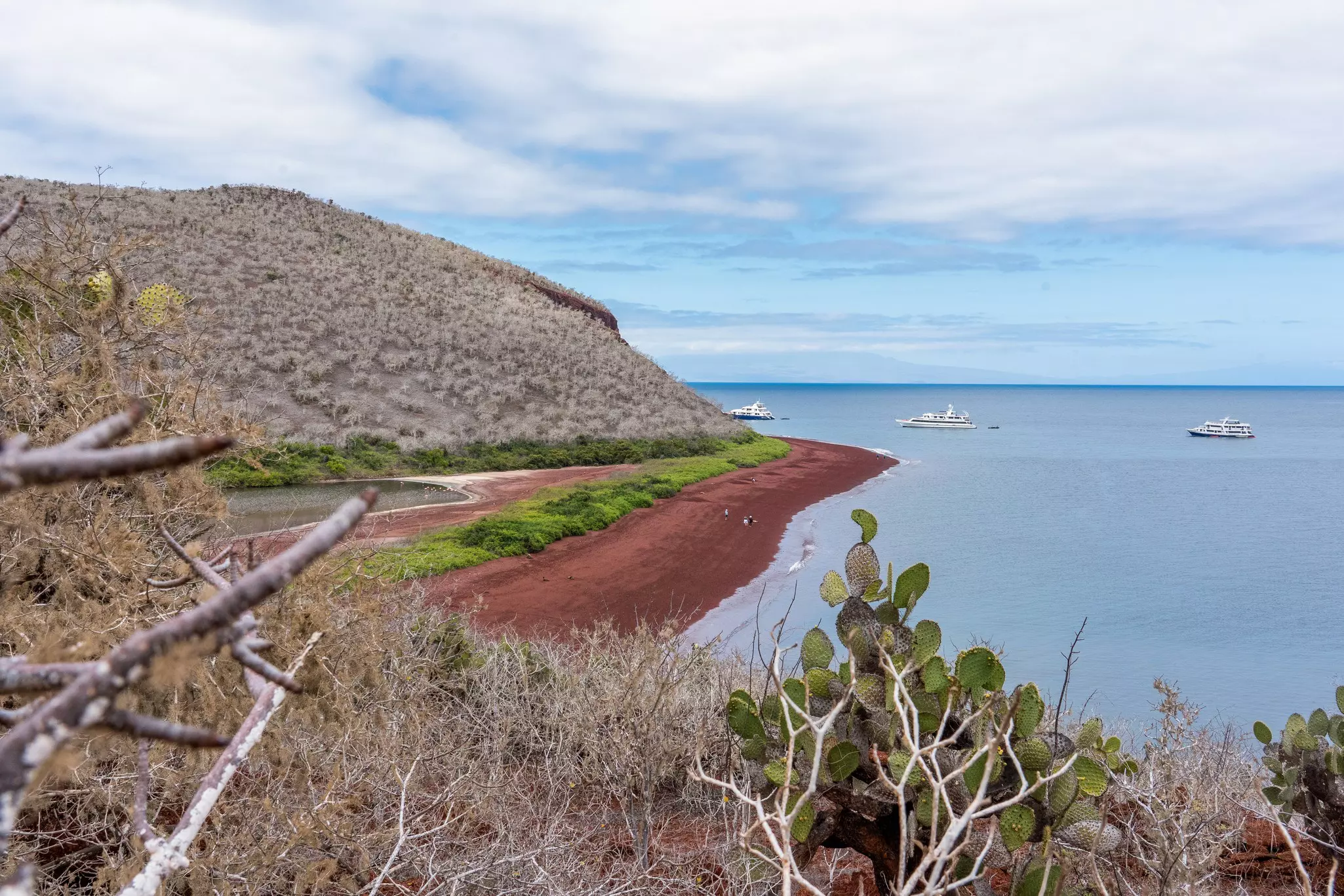 A viewpoint on Rábida Island looks out over the red beach and three liveaboard ships including the Integrity (center) © Sebastian Modak / Lonely Planet