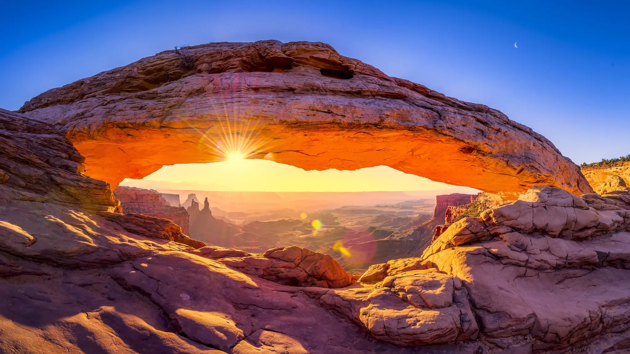 Close-up of Mesa Arch, a red canyon arch, at sunrise with a wide view into rocks and canyons beyond in Canyonlands National Park.