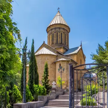 Sandstone church with a conical-roofed central drum, cypress trees, steps and an open wrought-iron gate