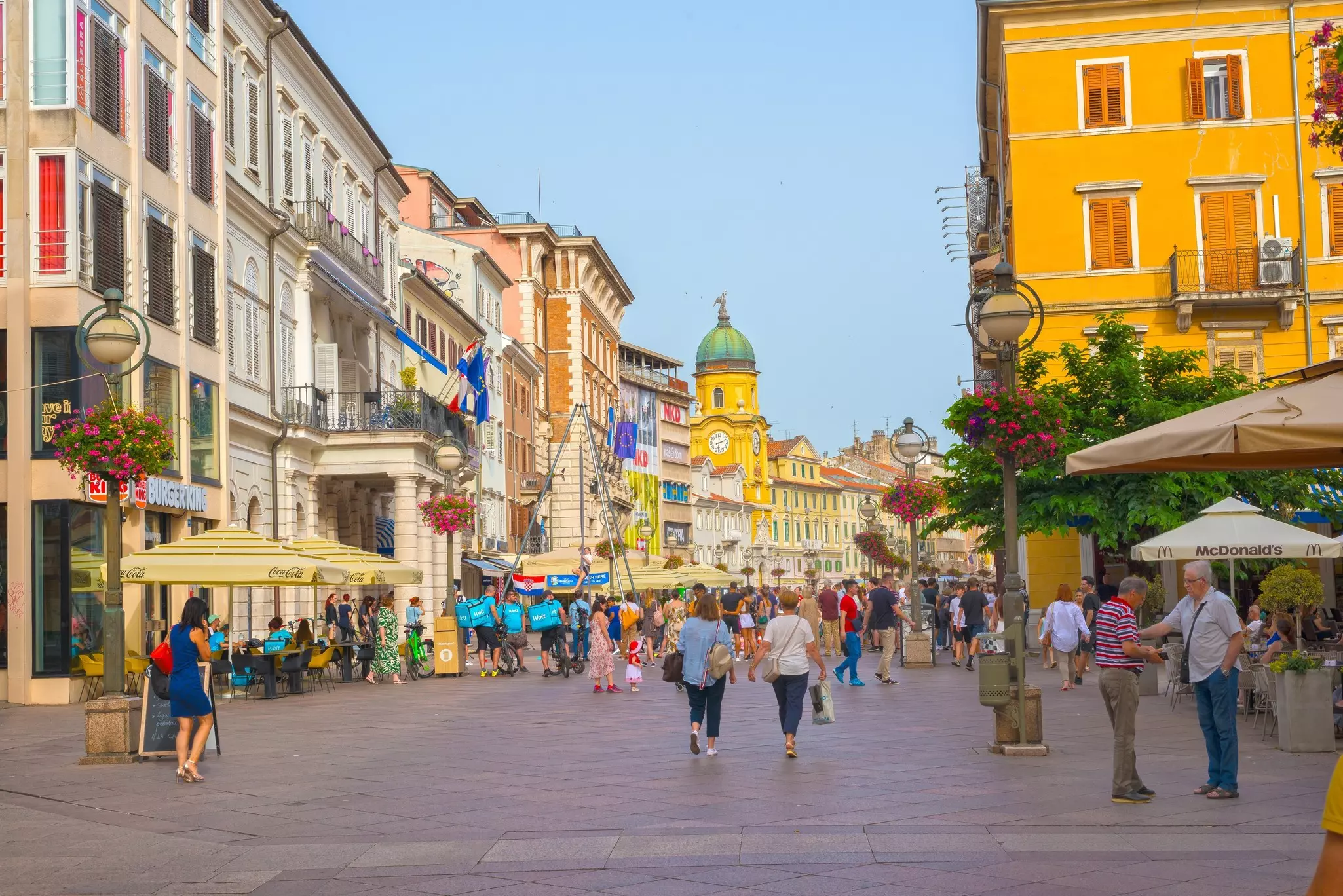 People walk along a street with sidewalk cafes in a historic city center in Croatia.