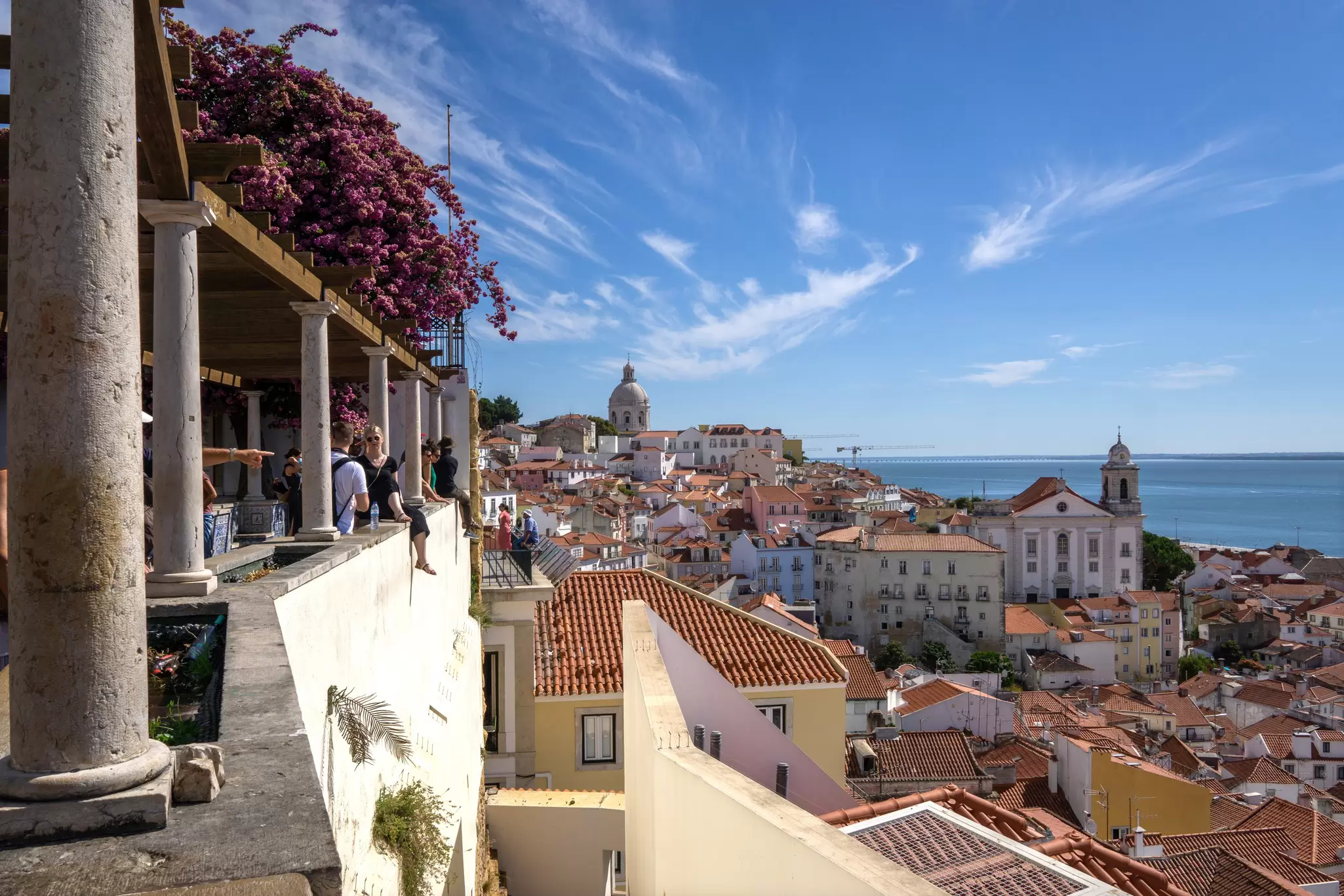 People at a viewpoint over red roofs of a hilly city