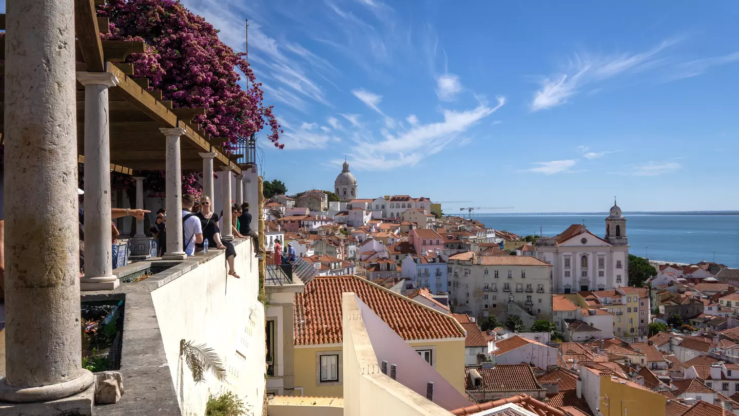 People at a viewpoint over red roofs of a hilly city
