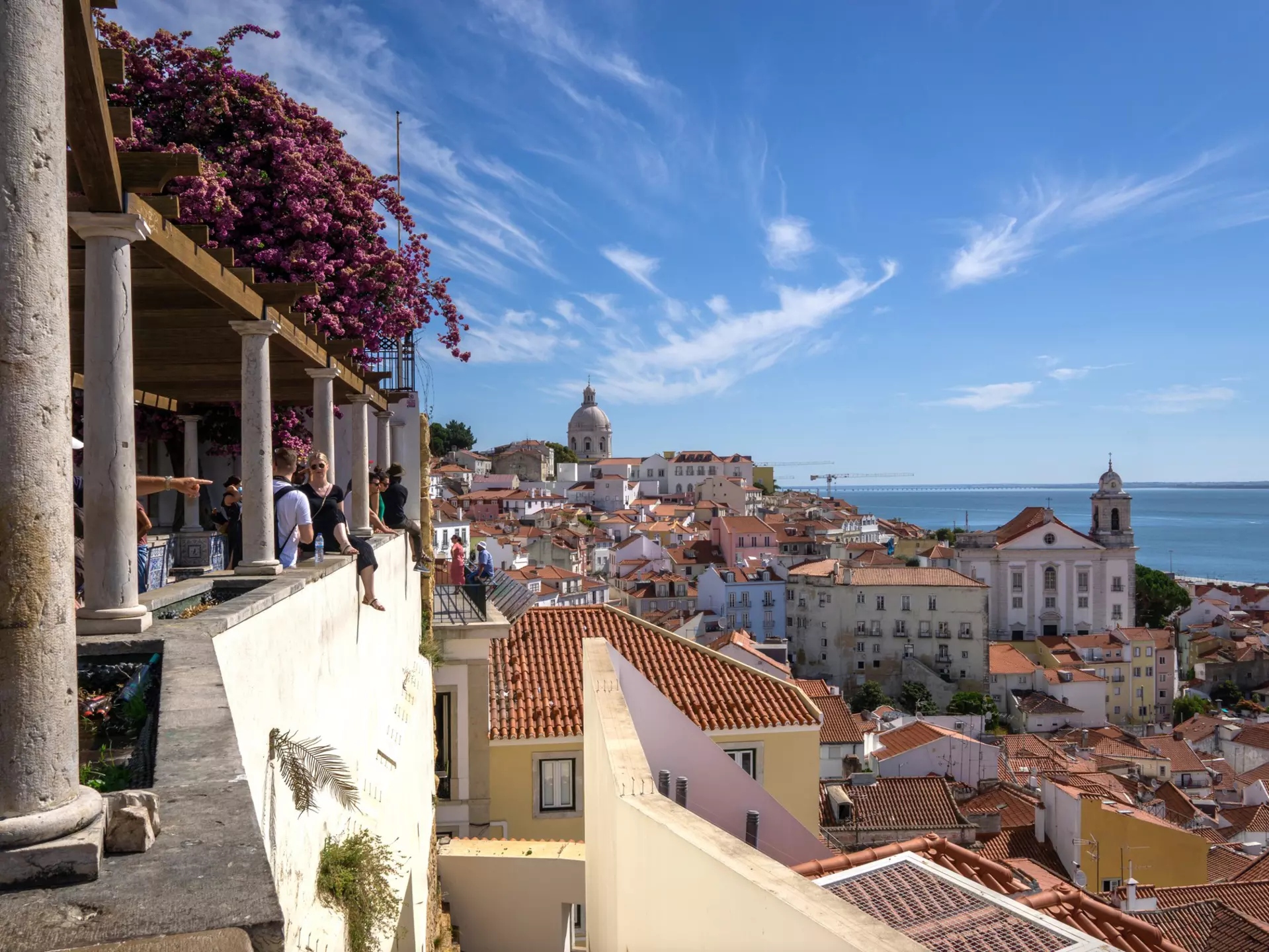 People at a viewpoint over red roofs of a hilly city