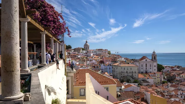 People at a viewpoint over red roofs of a hilly city