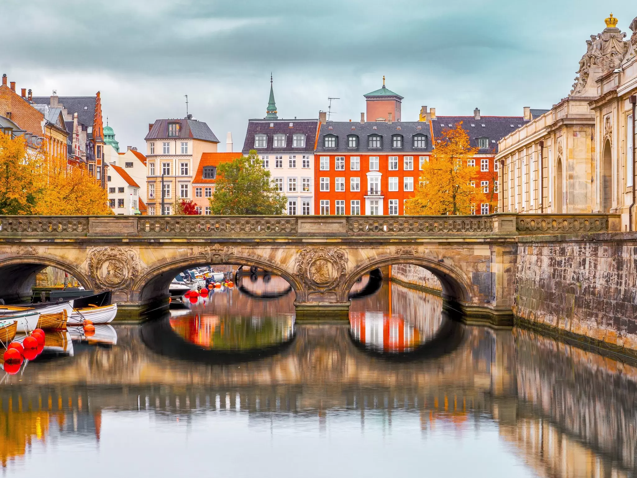 A river runs through the center of the city of Copenhagen, with trees whose leaves have turned golden in the autumn season