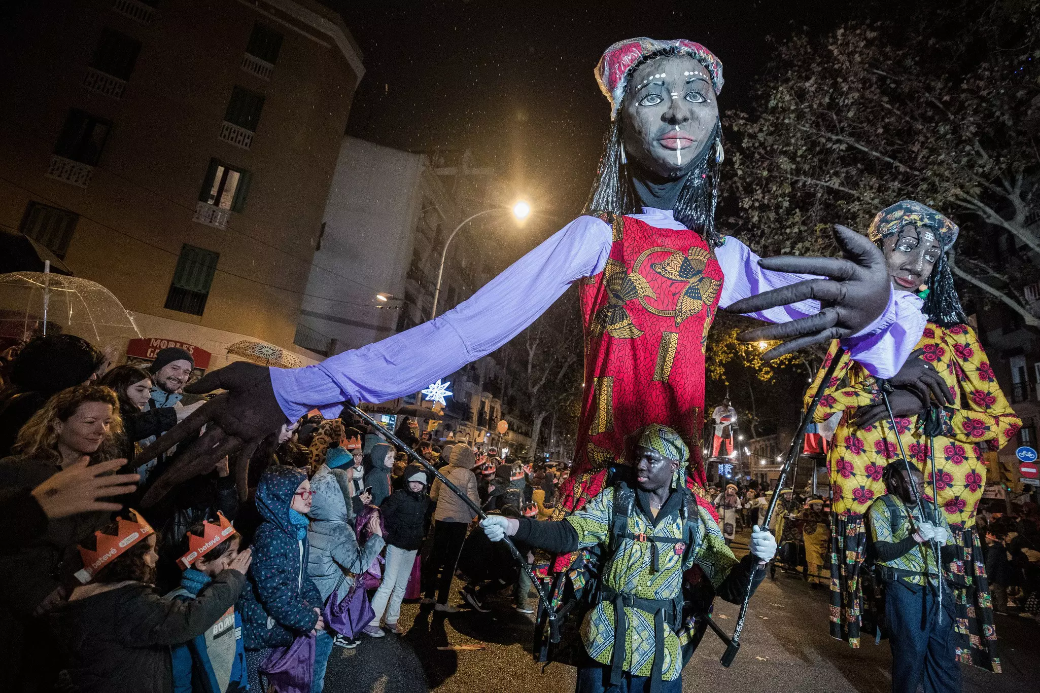 A man operates a large puppet during a parade a night in a city.