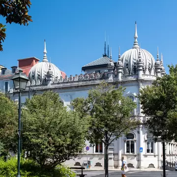 White neo-Moorish palace with onion domes and spires behind leafy trees and a lamppost in Principe Real, Lisbon.