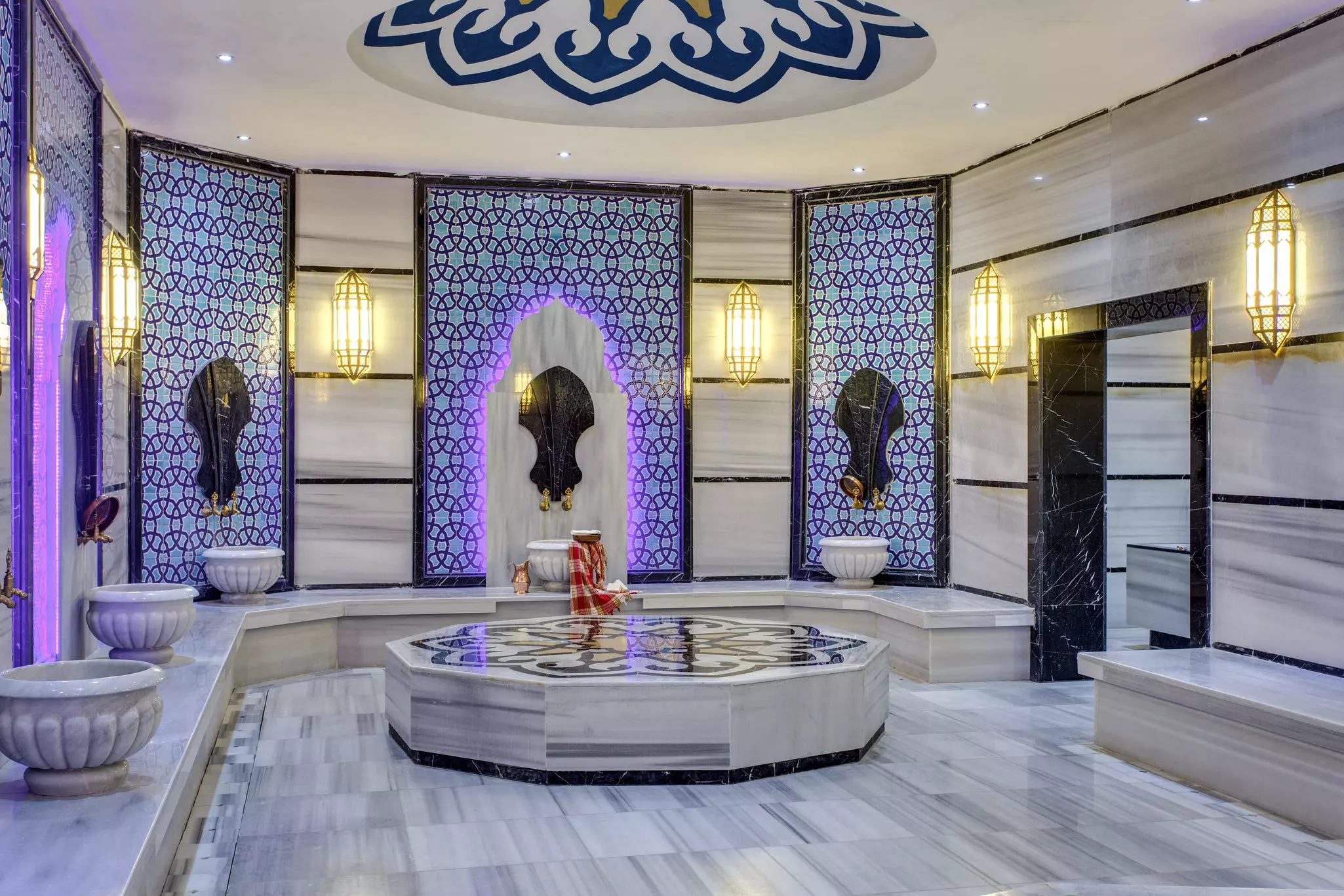 A marble room with built-in benches along the perimeter and a large central platform; there are patterned alcoves on the wall, and black accents on the doorway and benches.