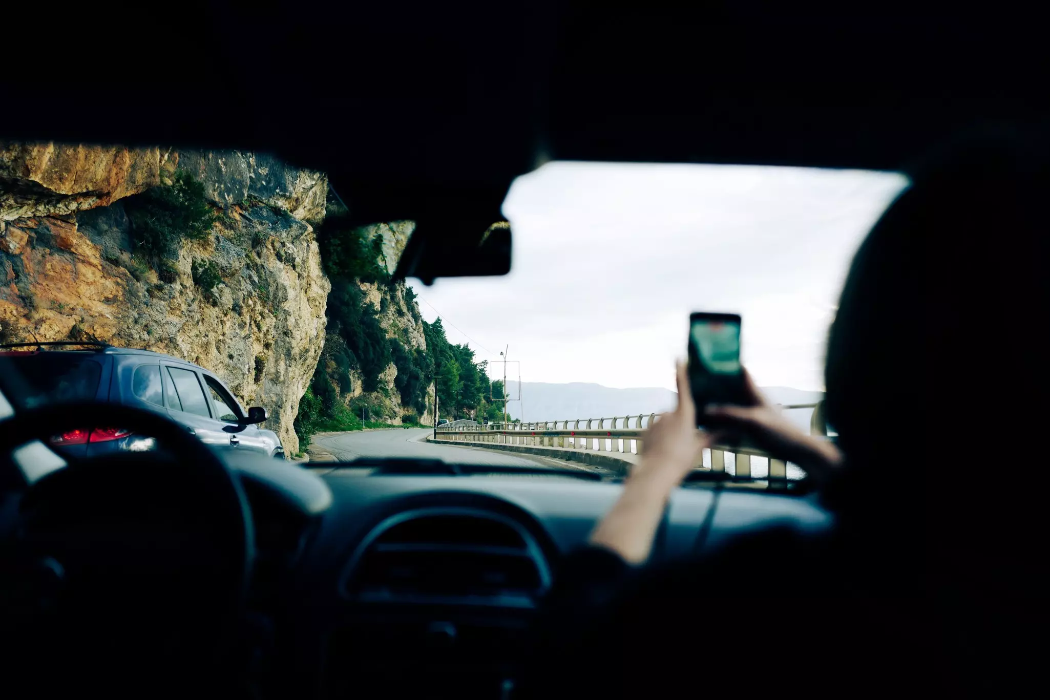 Woman holds up a phone camera inside a car on a roadtrip in Albania