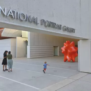 Concrete facade lettered National Portrait Gallery in Canberra, with visitors and a child running on the forecourt