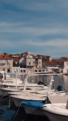 boats line a stone dock with stone buildings with red roofs in the background
