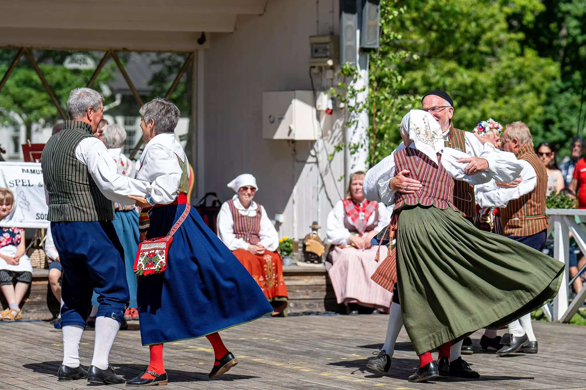 Elderly people in traditional costumes dance on a wooden platform.