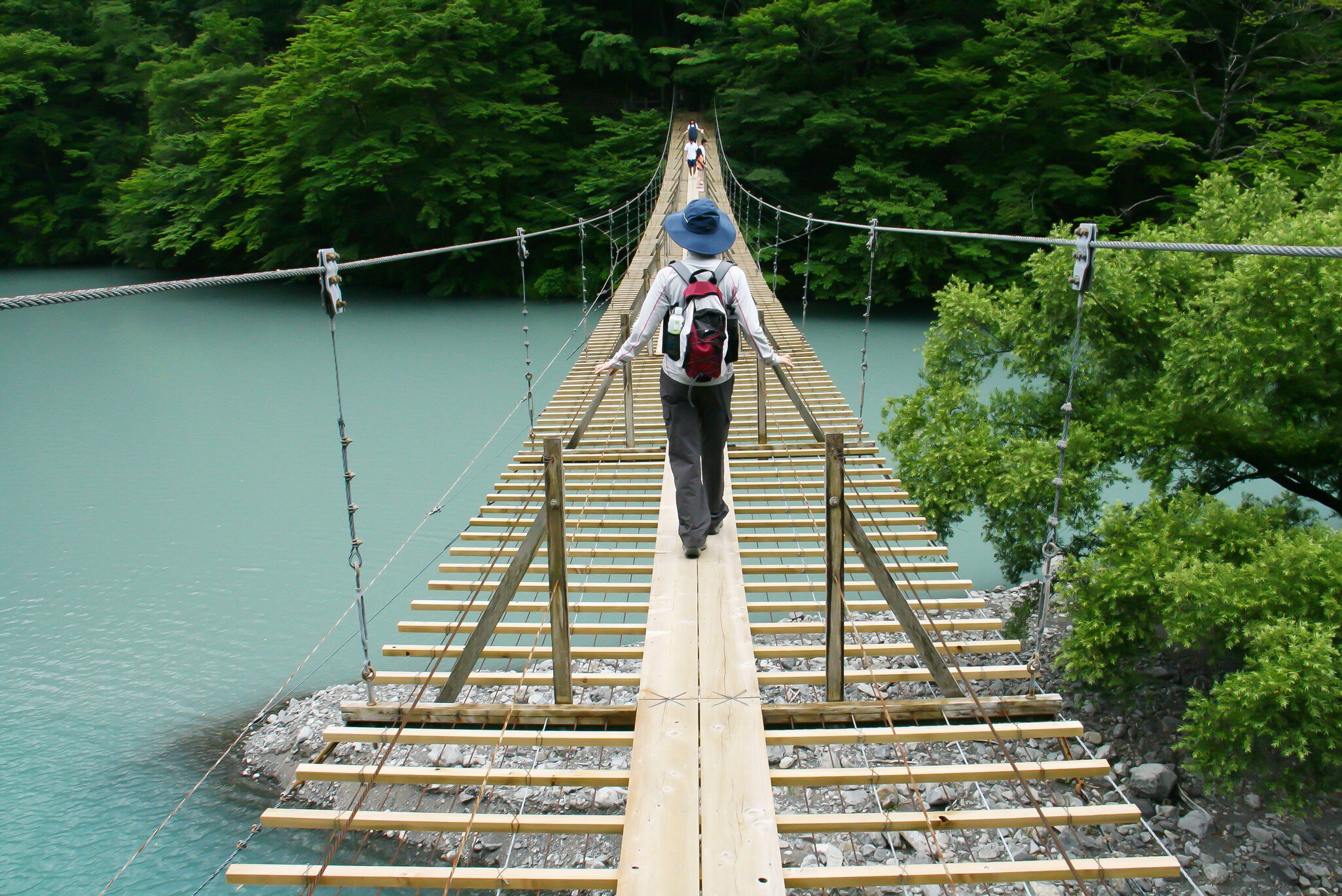 A person crosses a bridge over a light blue body of water.