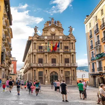 People wander through a city square lined with buildings.