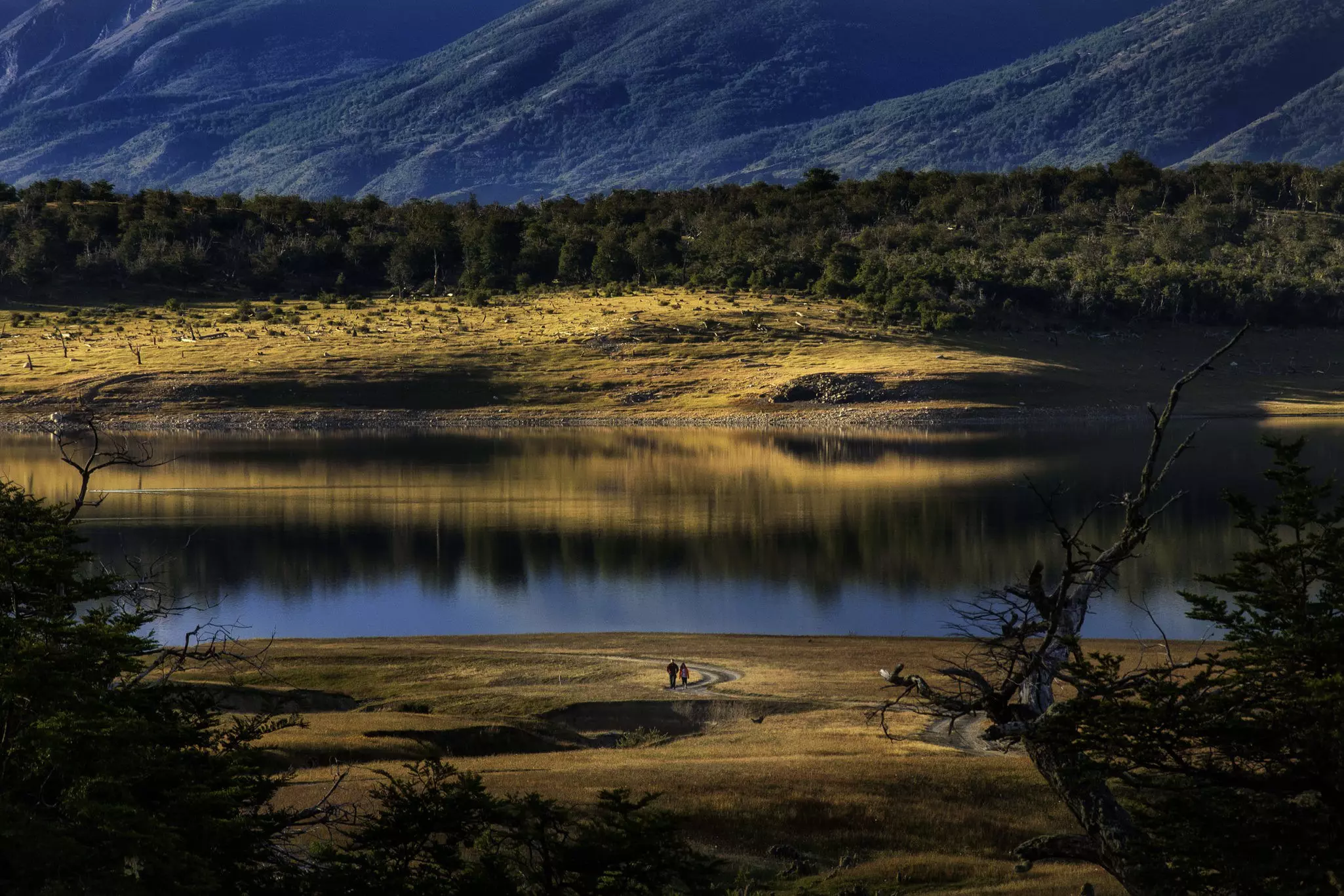 A couple walk along an empty dirt track at Roca Lake during sunset.