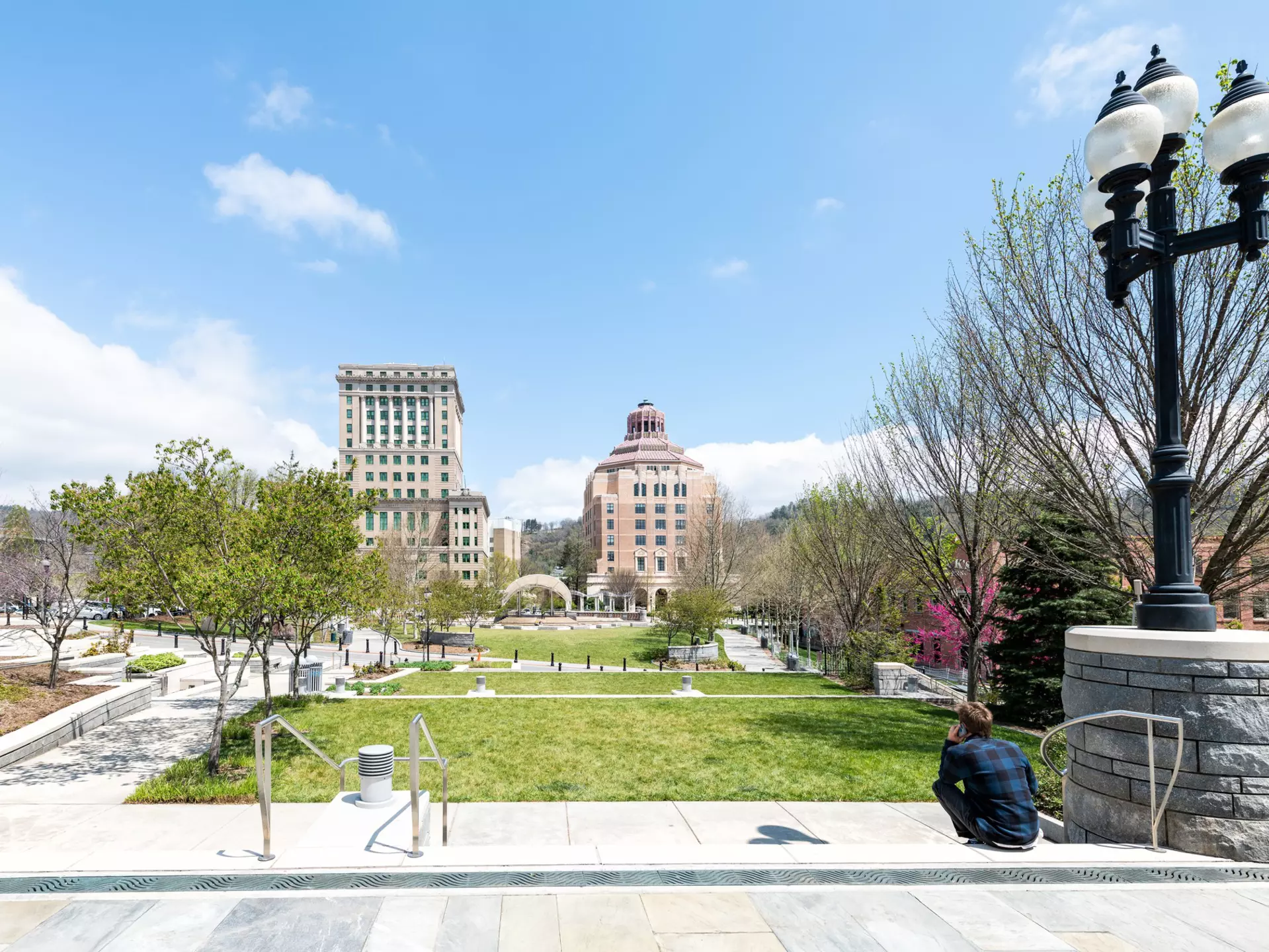 Back of young hipster millennial man sitting looking at buildings, courthouse and green Pack Square Park in hippie North Carolina NC famous town, city in the mountains, talking on phone