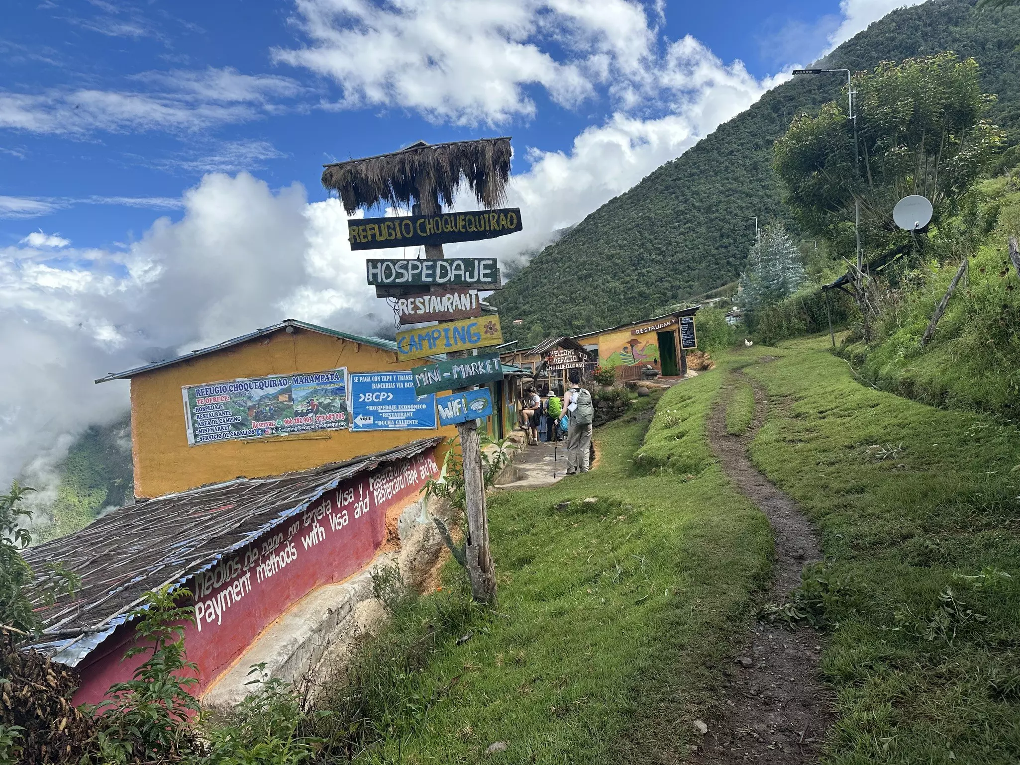Small structures in a village on the side of a lush green mountain under blue skies in Peru