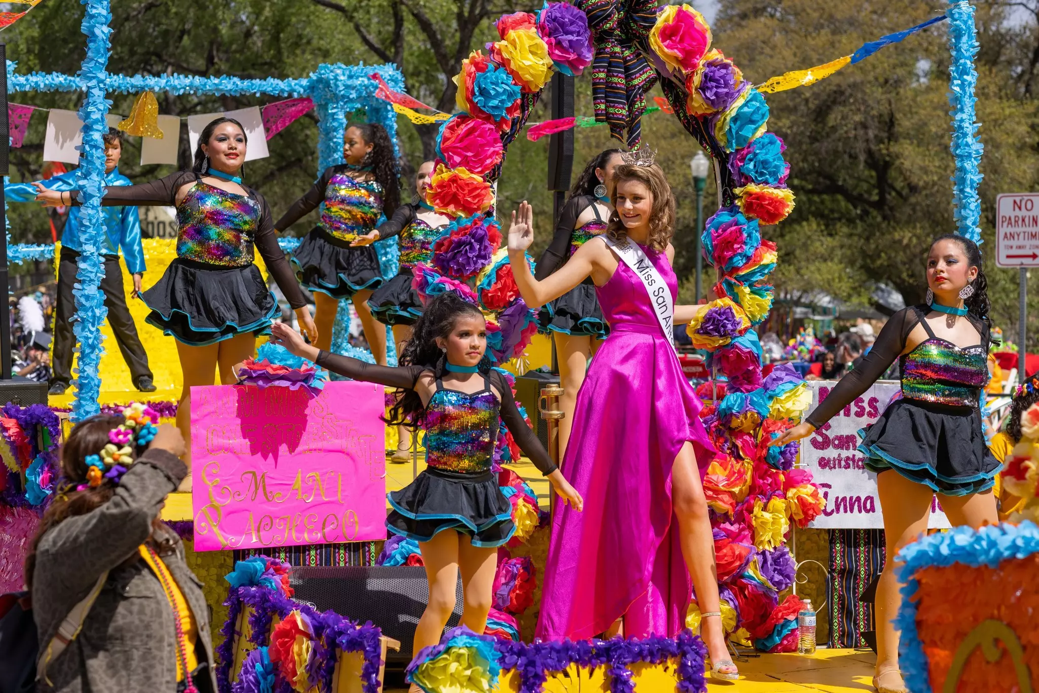 A beauty queen and young girls stand on a colorful float in a parade.