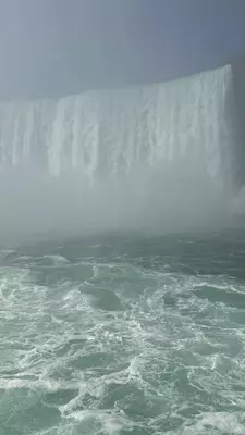 Falls from above with Rainbow arching over red Maid of the Mist boat. 
