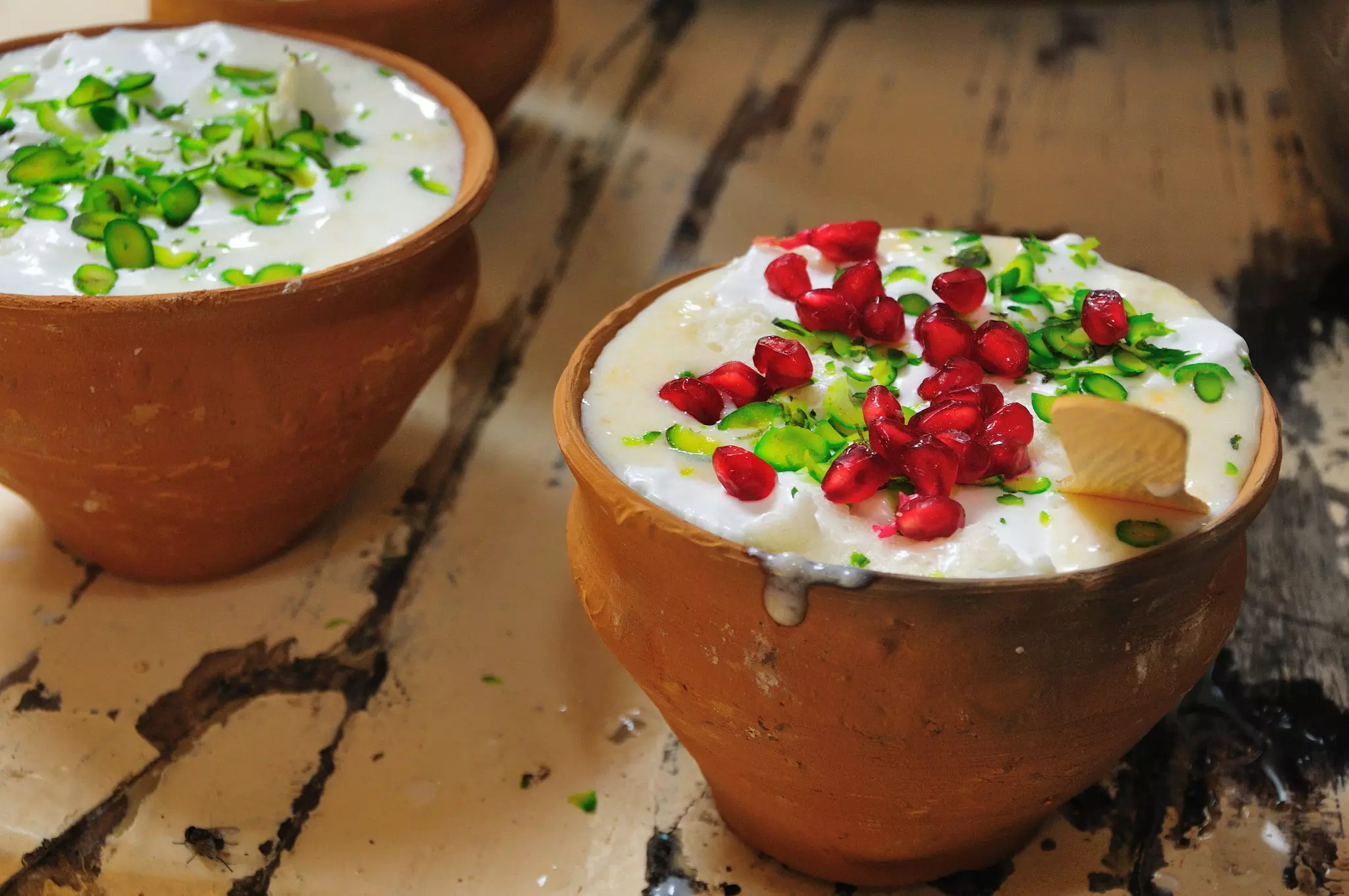 Two lassis in traditional clay pots, one topped with pomegranate seeds